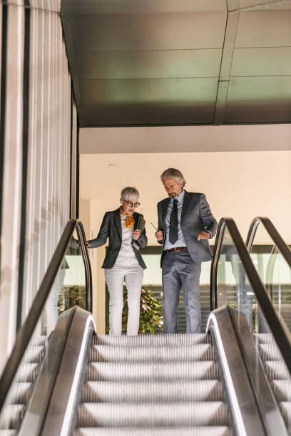 istock Business people moving down the escalator 1390254238