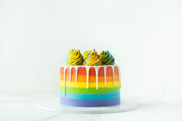 Photo of Rainbow cake with whipped cream top on the white background. Birthday cake with multicolored cream cheese frosting