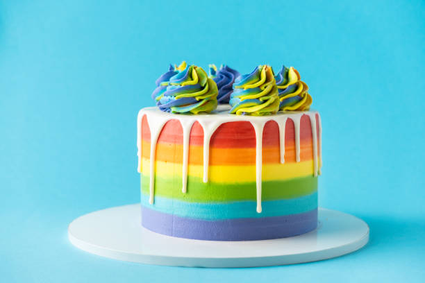istock Rainbow cake with whipped cream top on the blue background. Birthday cake with multicolored cream cheese frosting 1390254322