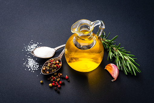 Cooking and seasoning: high angle view of an extra virgin olive oil bottle and two spoons with peppercorns and salt shot on dark background High resolution 42Mp studio digital capture taken with Sony A7rII and Sony FE 90mm f2.8 macro G OSS lens