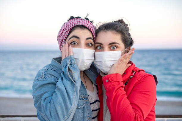 istock Two girlfriends wearing protective face masks hug each other on the beach and are scared, the new normal 1390258634