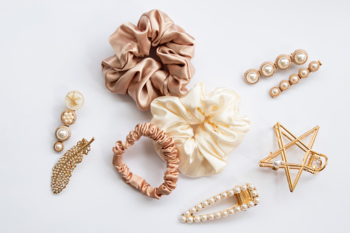 Collection of trendy silk elastic band scrunchies and pearl hair clips on white background. Diy accessories and hairstyles concept, luxury color