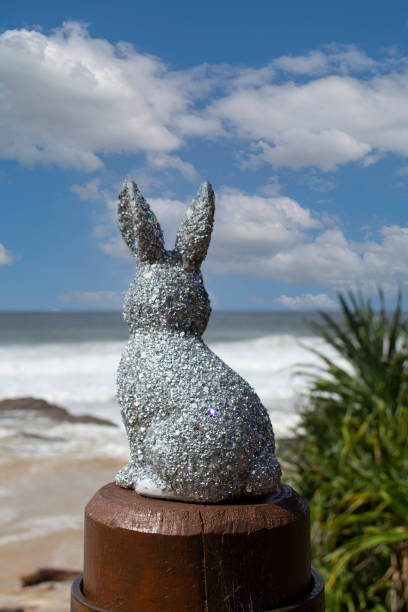 istock Silver sparkly glitter Easter Bunny at the beach.  Sitting on a brown post looking out to the ocean. Ocean & sky in the background with Pandanus trees down below. Gold Coast Queensland Australia 1390265948