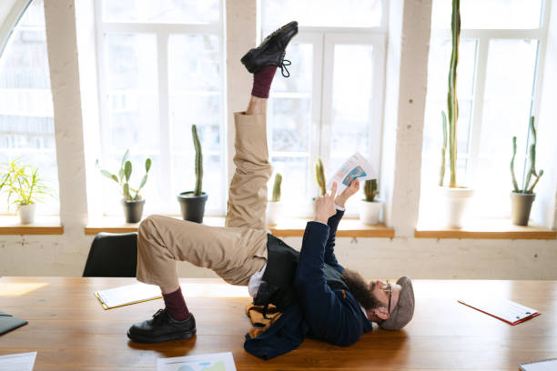 istock Young bearded man, office clerk having fun, doing yoga on wooden table in modern office at work time with gadgets. Concept of business, healthy lifestyle, sport, hobby 1390270251
