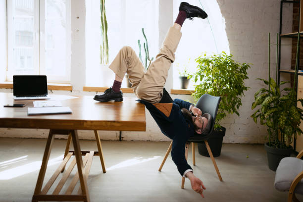 istock Young bearded man, office clerk having fun, doing yoga on wooden table in modern office at work time with gadgets. Concept of business, healthy lifestyle, sport, hobby 1390270280