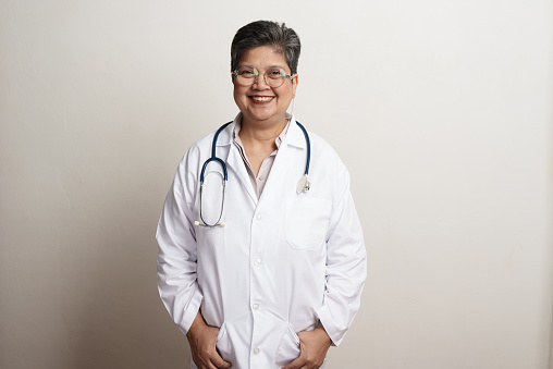 Portrait of senior Asian doctor with eyeglasses standing against white background. Female doctor smiling and looking at camera. studio portrait advertising banner concept.