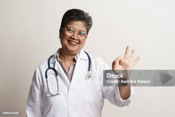 Portrait Of Confidence Senior Asian Woman Doctor Standing Against White Background Stock Photo - Download Image Now