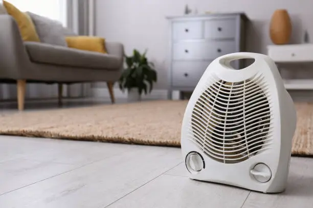 Modern electric fan heater on floor at home. Space for text