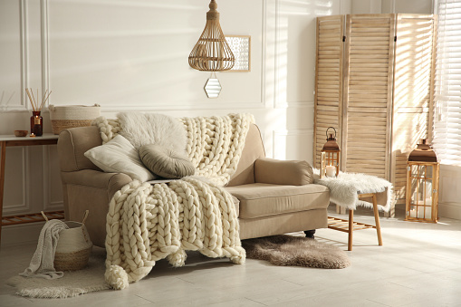 Acogedor interior de sala de estar con sofá beige, manta de punto y cojines photo