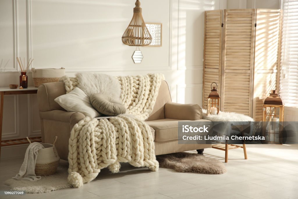 Cozy living room interior with beige sofa, knitted blanket and cushions Living Room Stock Photo