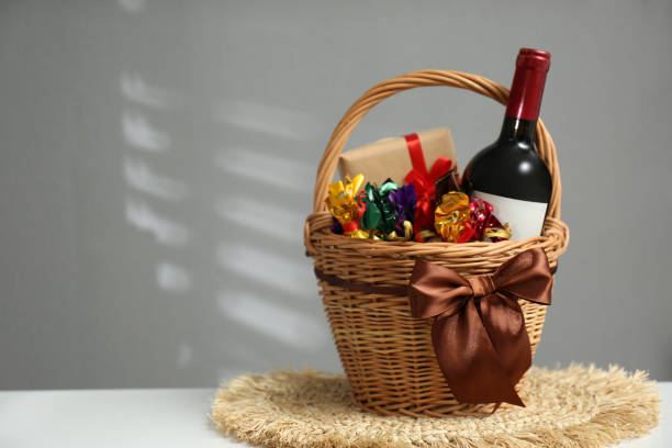 istock Wicker gift basket with food and wine on white table against grey background. Space for text 1390278585