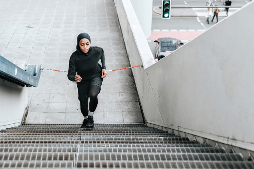 young sports woman with sports hijab running up stairs outdoors in berlin