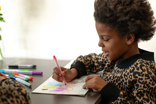 African-American girl are drawing with felt-tip pens together with her caucasian mother at home.Diverse people.Time together.Selective focus,close up,copy space.