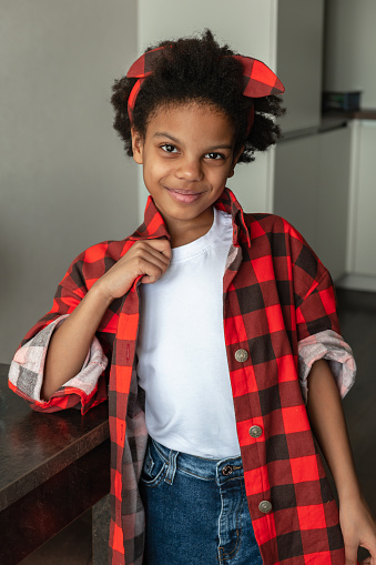 Portrait of a cute 9-year-old African-American girl in a red shirt and jeans at home.Diverse people.
