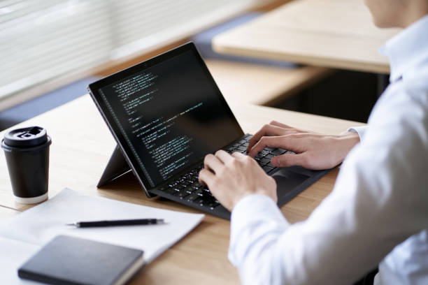 asian programmer writing code on a laptop - hot desking imagens e fotografias de stock