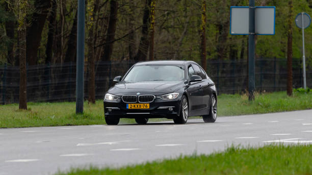 Enschede, Twente, Overijssel, Netherlands, april 5th 2022, Dutch black 2013 BMW 6th generation 3-series sedan '3L' approaching on the 'Hengelosestraat' city street in Enschede on a rainy day - the 3-Series is a line of executive cars made by German, Munich based automaker BMW since 1975