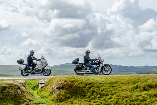Two male motorcyclists riding on moorland road across Dartmoor National Park