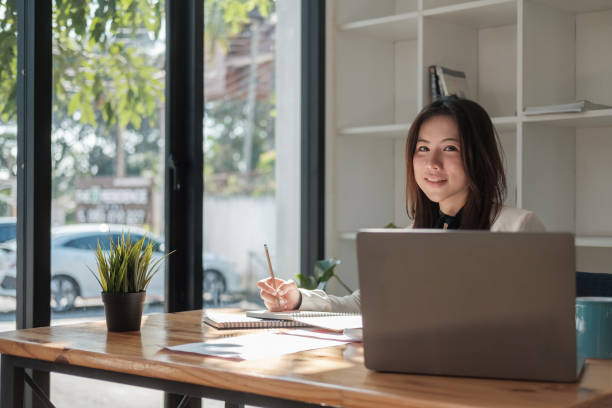 istock Charming Asian woman with a smile working for financial marketing plan using laptop computer 1390292828