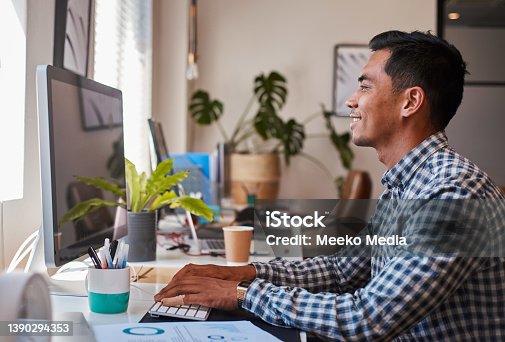 istock A young Asian businessman types at his desk on the computer while smiling 1390294353