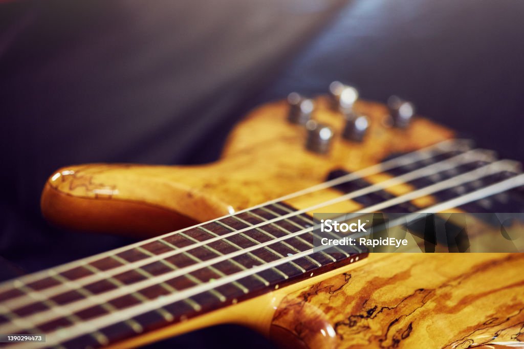 Detail of a beautiful bass guitar with an intricate wooden top made of spalted maple Electric bass guitar resting on a leather couch. Bass Guitar Stock Photo
