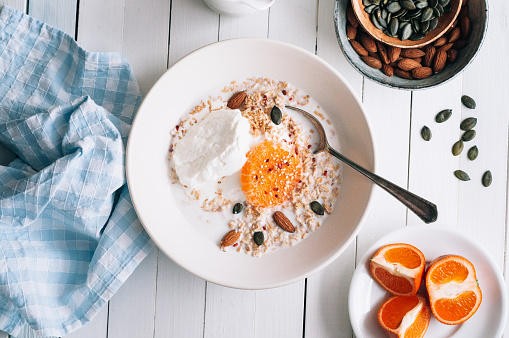 Oatmeal with curd cheese and tangerine on a white plate standing on a table