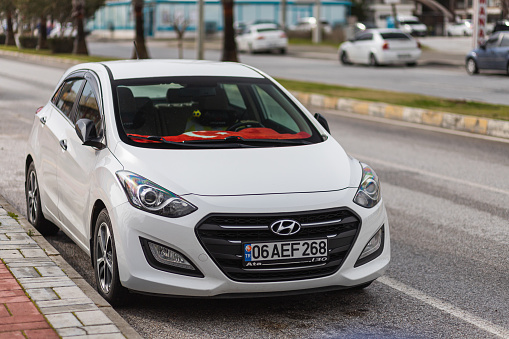 Side, Turkey -January 25, 2022: white Hyundai i20  is parked  on the street on a warm summer day against the  road and trees