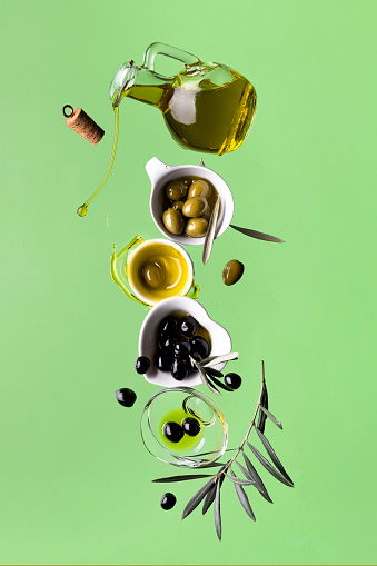 extra virgin olive oil and olives, composition in balance, still life in motion. green background