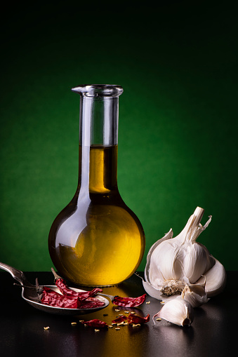 in the foreground a glass cruet with Italian extra virgin olive oil, garlic and dried chilli. still life