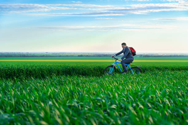 a businessman rides a bicycle with a backpack through a green grass field, dressed in a business suit, beautiful nature in spring, business concept