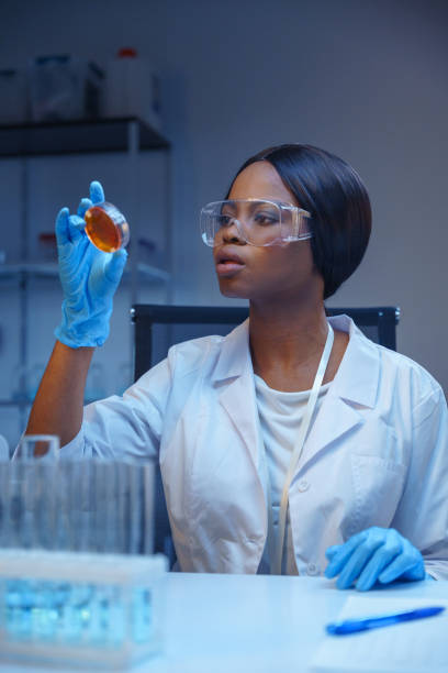 istock A  young beautiful African - American  bacteriologist in protective glasses and gloves looking at a Petri dish with bacterial growth 1390303424