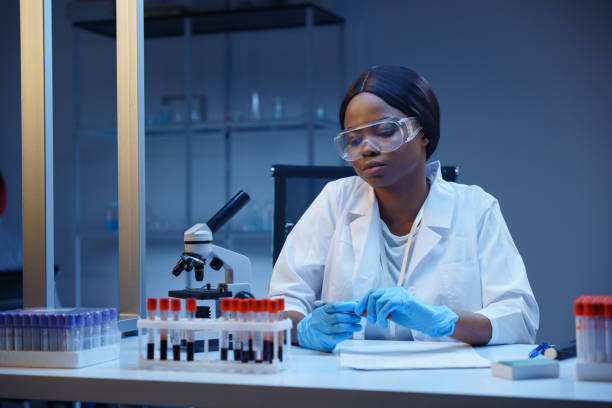 istock A young bored African-American lab worker working with test tubes with blood samples, sitting at her desk in a modern medical laboratory, conducting blood analysis 1390303525
