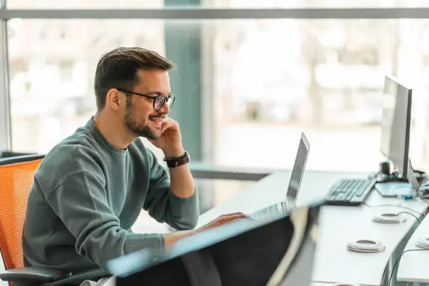 A young man is working on a computer in the bright office.