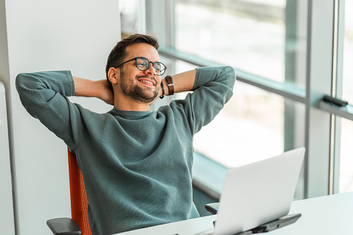 A young man is taking a short break from working on a computer in the bright office.