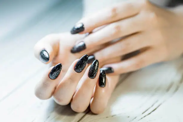 Photo of Gorgeous manicure, black nail polish with sequins, close-up photo. Women's hands on a simple background.