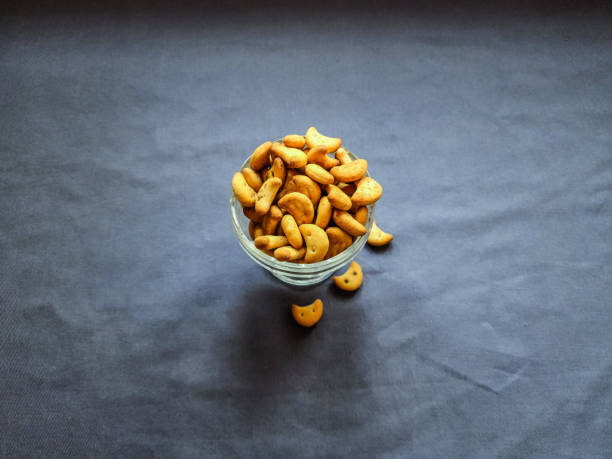 Stock photo of testy crunchy salted masala cashew shape biscuit kept in transparent glass bowl on dolphin gray color background. Picture captured under bright light at Bangalore, Karnataka, India. stock photo