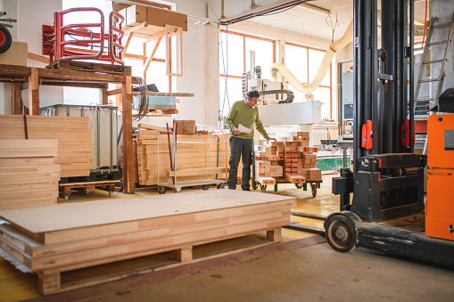 Senior adult Caucasian carpenter preparing wooden planks for work. Piling it next to a processing machine.