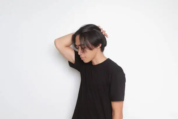 Portrait of handsome Asian man in black t-shirt with long hair. Model posing while straightening hair with hand. Isolated image on white background