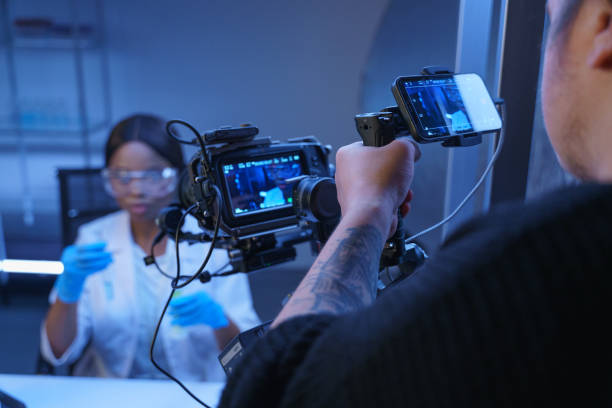 A professional camera shooting an African- American actress in a role of a scientist in a laboratory. Backstage from filming a movie of a photo set in a laboratory decorations and an operator shoulder in the foreground una cámara profesional fotografiando a una actriz afroamericana en un papel de científico en un laboratorio. backstage de la filmación de una película de una foto ambientada en las decoraciones de un laboratorio y un hombro de operador en primer plano