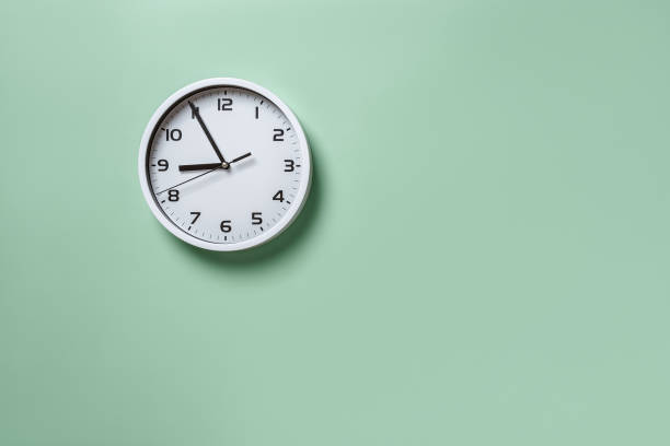 Wall clock hanging on the pale green wall with copy space. Round white clock with black hands. Five minutes to nine. Time measuring, hour and minutes concepts. Time control. Working hours.
