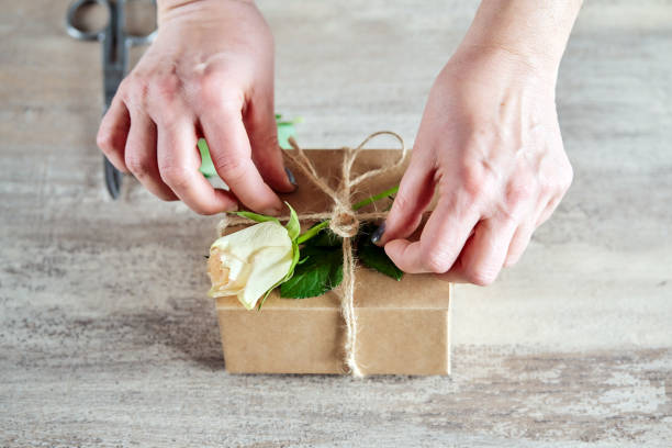 istock Female hands preparing a gift box with white rose on wooden background 1390324472