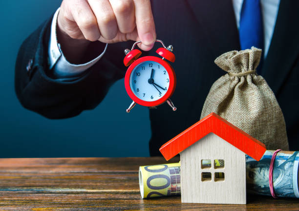 real estate agent holding a clock over the house. limited offer. rental business. special offers for buying a home. making a mortgage loan. seasonal sale. investment in housing with further profitable rental. - stock market data insurance savings finance imagens e fotografias de stock