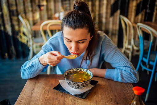 Young woman eating vegetable soup at restaurant