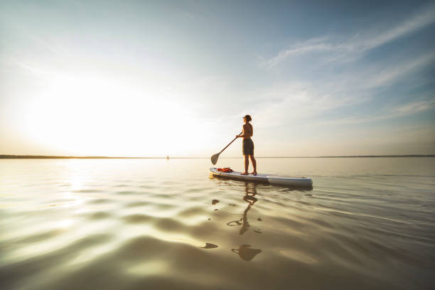 Giovane donna che nuota sulle tavole da sup da sola al tramonto - foto stock