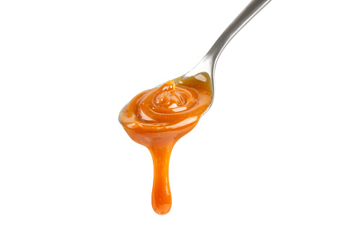 Liquid caramel on spoon. Caramel drips from the spoon. Pouring sweet caramel sauce. Texture, Close up.