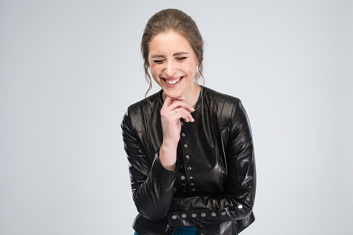 Beautiful caucasian woman in the black leather jacket and dark turquoise dress at the studio with light gray background. Copy space for your design.