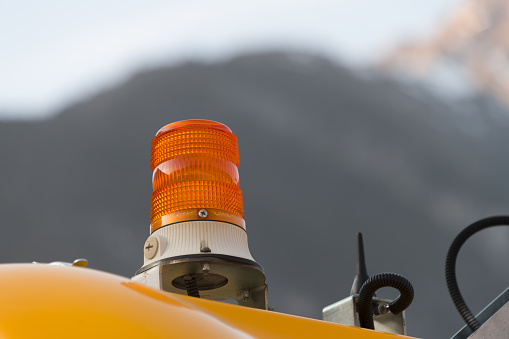 Close up of orange yellow rotating beacon torch lamp as warning light when using work machines and equipment in front of mountains and blue sky