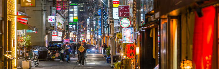 People and traffic in the neon lit alleyways of the Umeda district between the restaurants and bars of downtown Osaka, Japan’s vibrant second city.