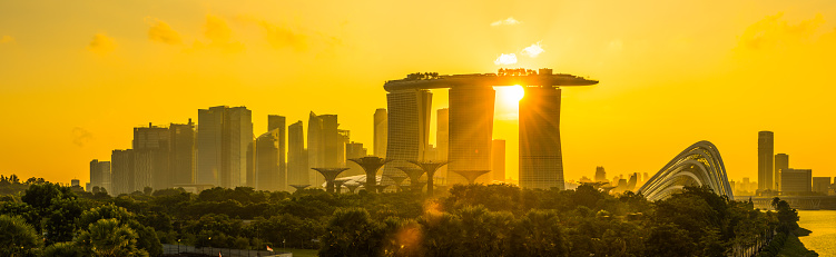 Golden sunset light silhouetting the skyline of Singapore, from the crowded skyscraper cityscape of the Central Business District to the iconic pillars of the Marina Bay Sands.