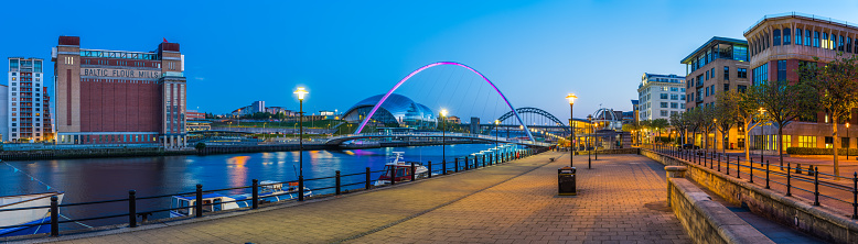 Modern developments overlooking the Millennium Bridge and the Newcastle Upon Tyne quayside illuminated at dusk, UK.
