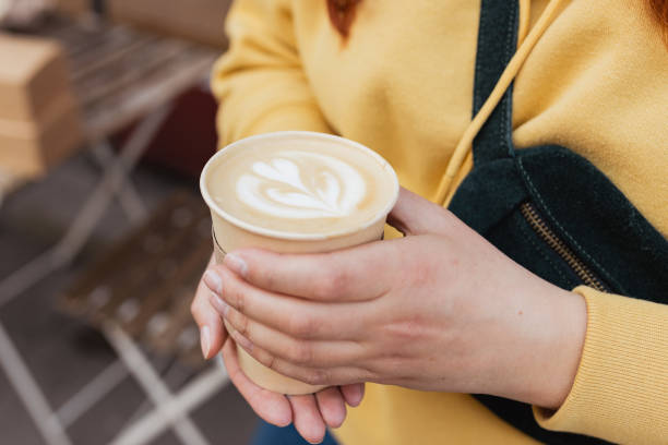 Bio paper cup with coffee latte art in woman hand. Young stylish hipster redhead girl drinking hot latte. Traveler. Take away delivery concept. Eco recycle environment friendly. Bio paper cup with coffee in woman hand. Young stylish hipster redhead girl drinking hot latte. Urban lifestyle banner. Take away delivery concept. Eco recycle environment friendly. paper coffee cup stock pictures, royalty-free photos & images